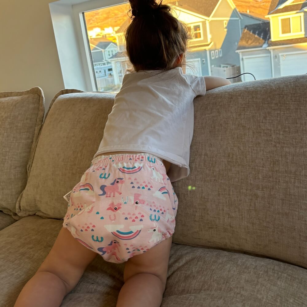  Kind lehnt sich ans Fenster in rosa Einhorn-Trainingshose auf einem Sofa